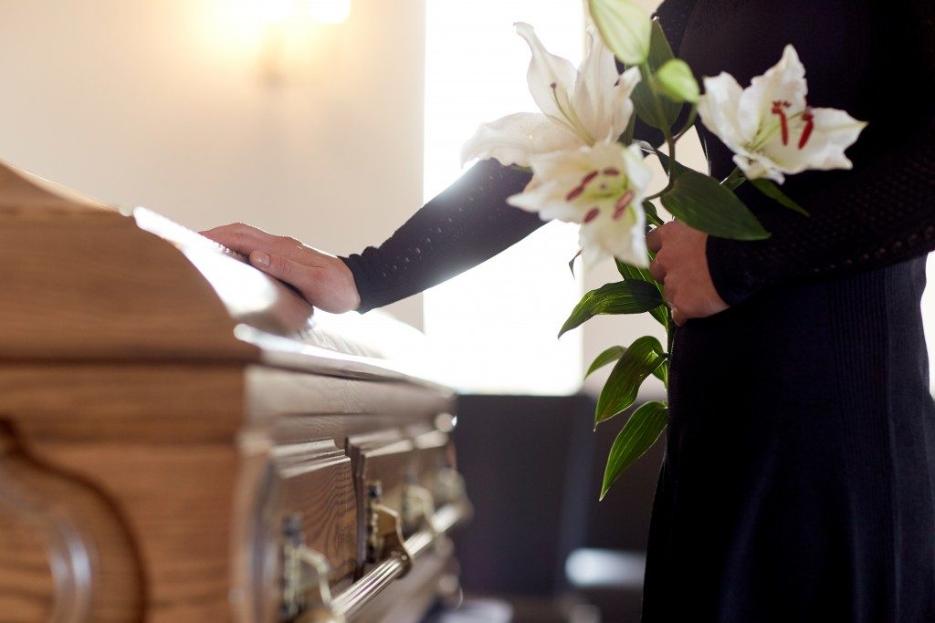 mourning woman holding a white flower beside a wooden coffin inside a chapel