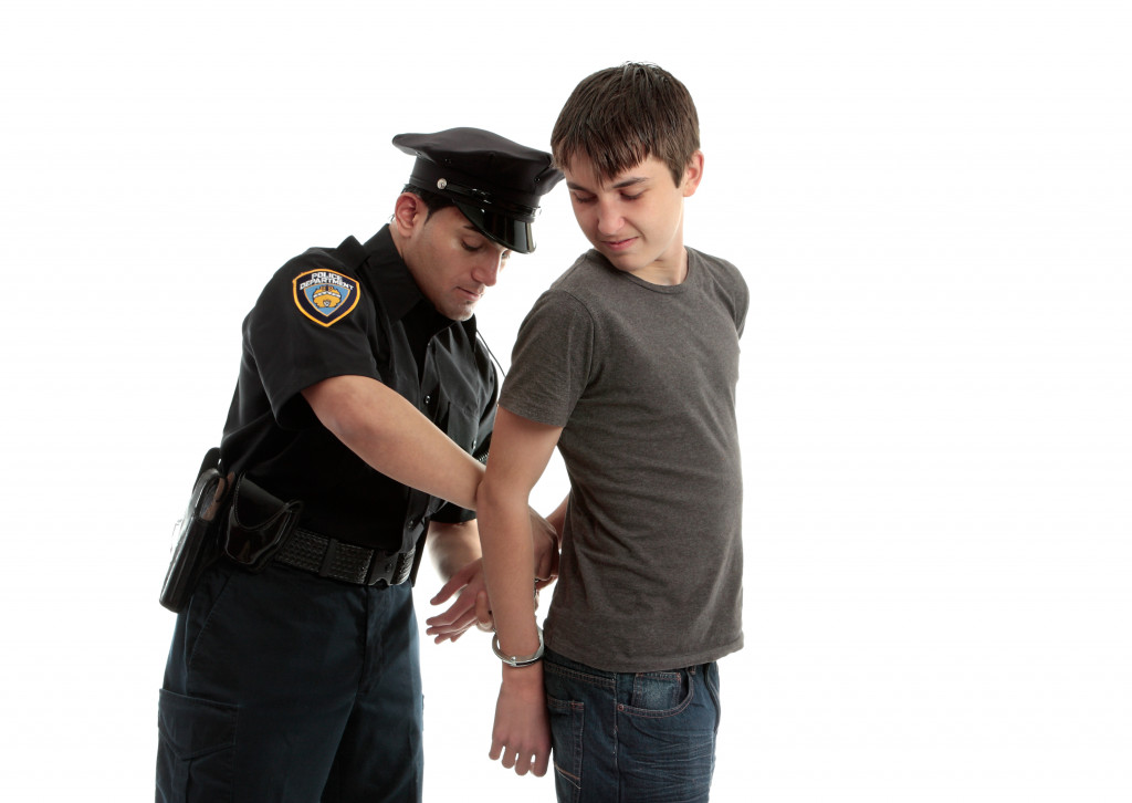 A police officer arrests and handcuffs a young male teen felon