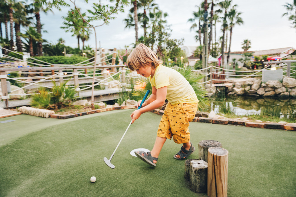 Young boy playing in a miniature golf course.