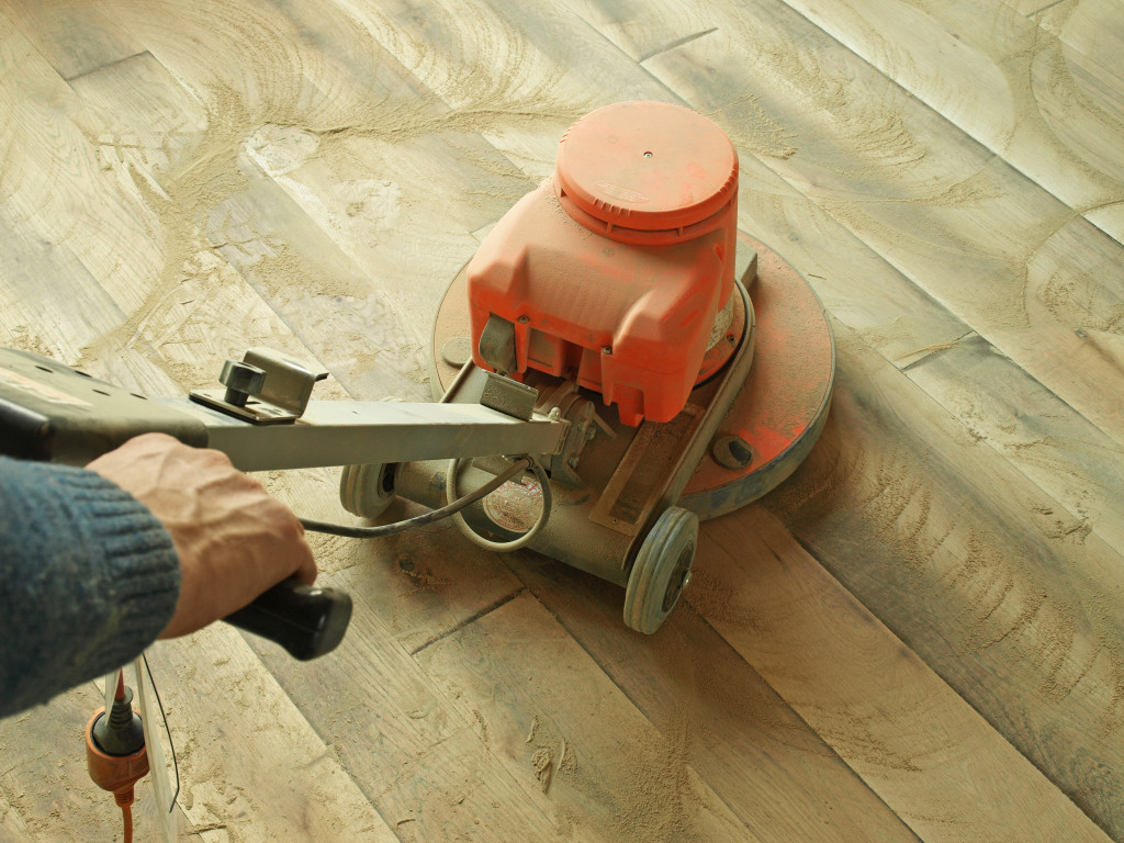 A person sanding a hardwood floor with an automatic sander