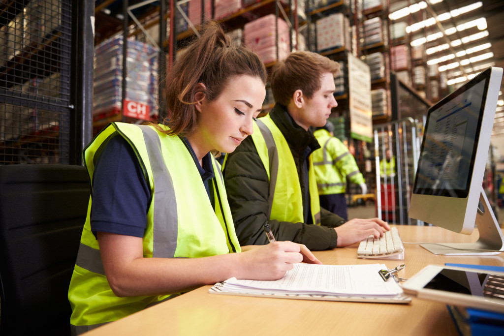 Two employees in a warehouse where one is taking notes of something