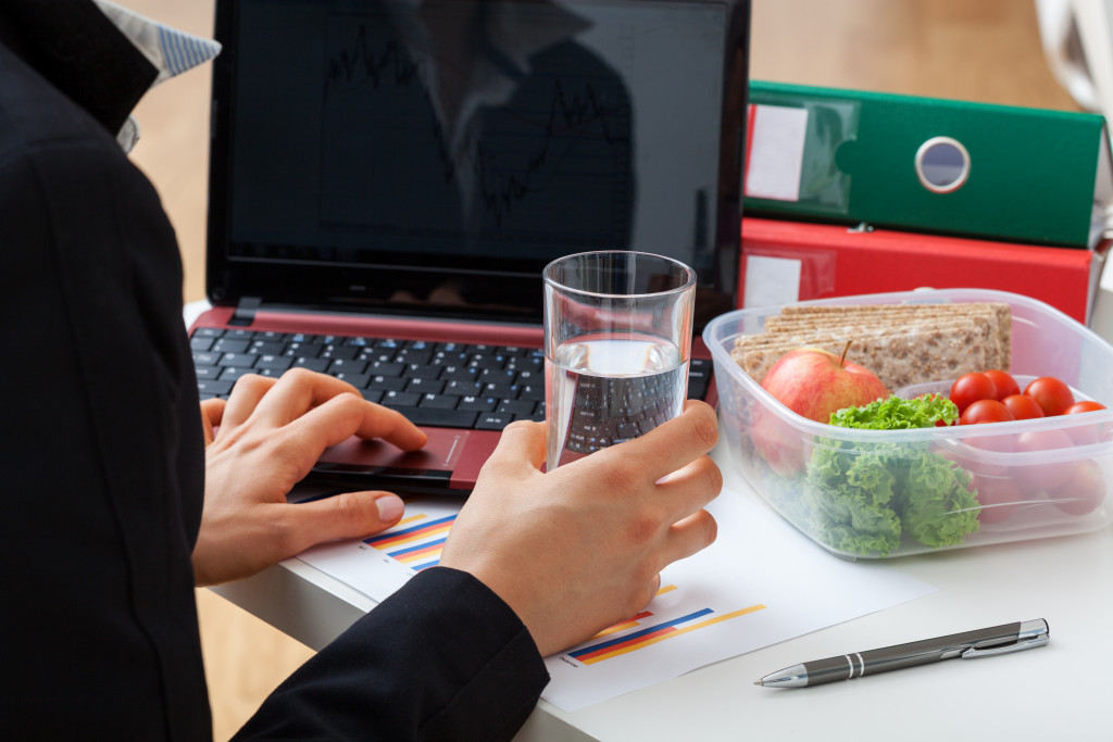 An office worker with a laptop, glass of water, and healthy food