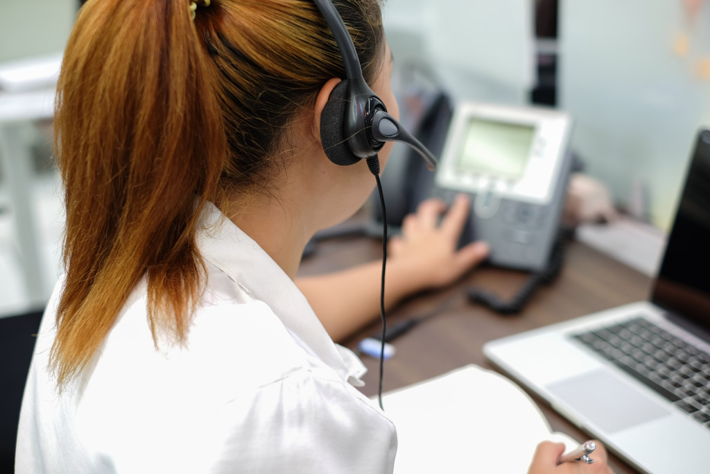 A woman answering the telephone while using a laptop and headset 