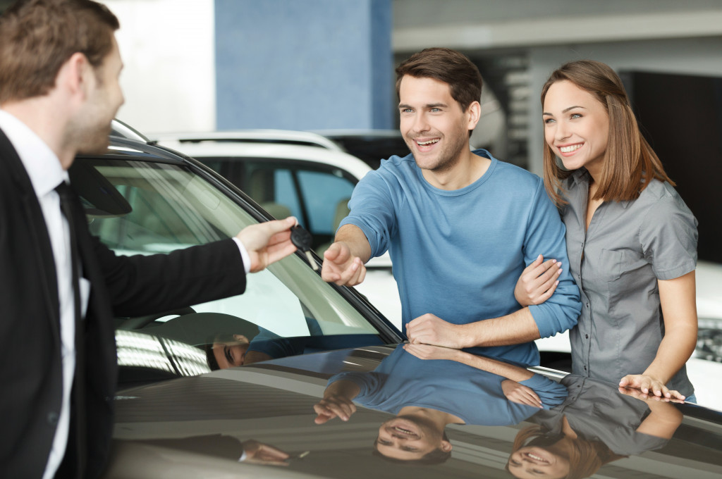 Executive giving the keys for a rental car to a young couple.