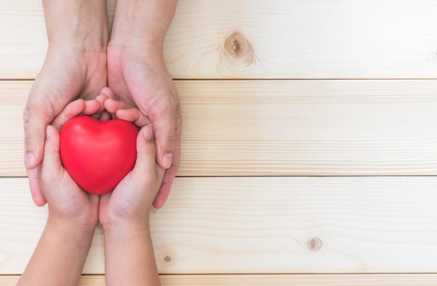 An adult's hands holding a child's hands that is holding a plastic heart.