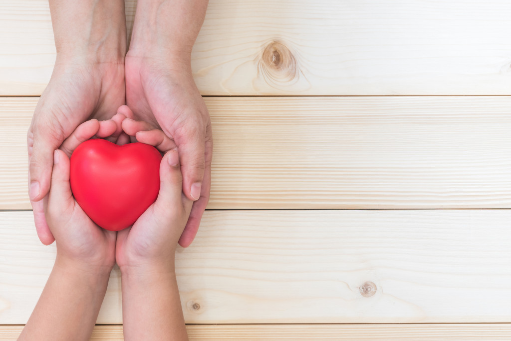An adult's hands holding a child's hands that is holding a plastic heart.