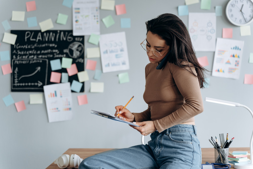 Businesswoman taking notes while talking on the phone in her office