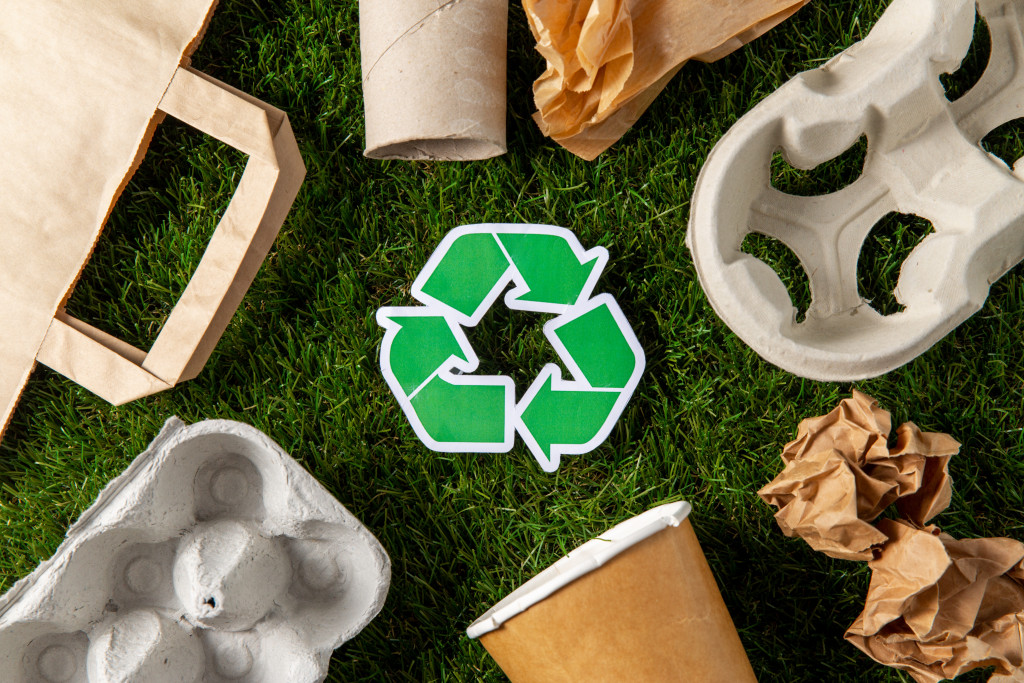 Close-up of green recycling sign and paper waste on grass