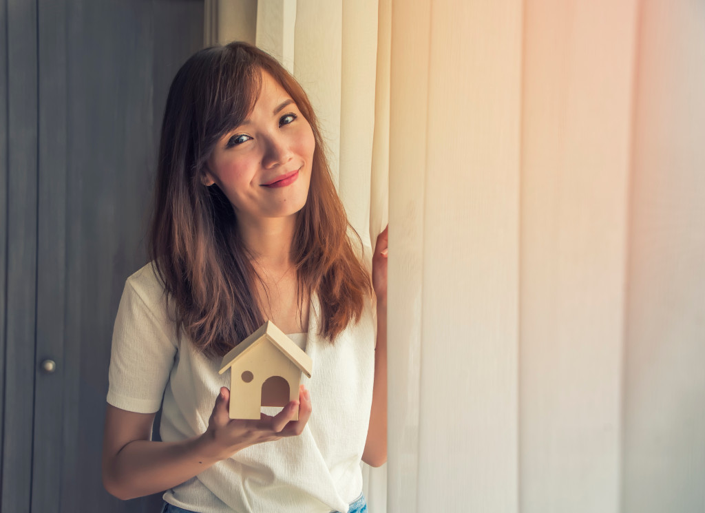 A female real estate agent holding a model house beside curtains