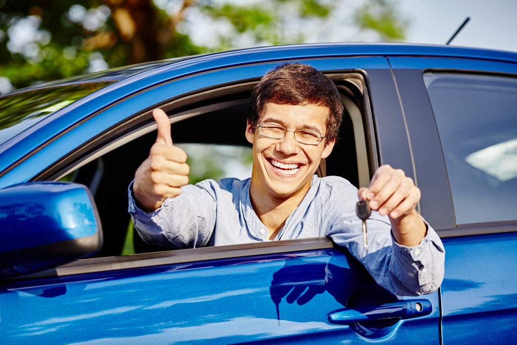A man holding his keys with a thumbs up inside his blue car