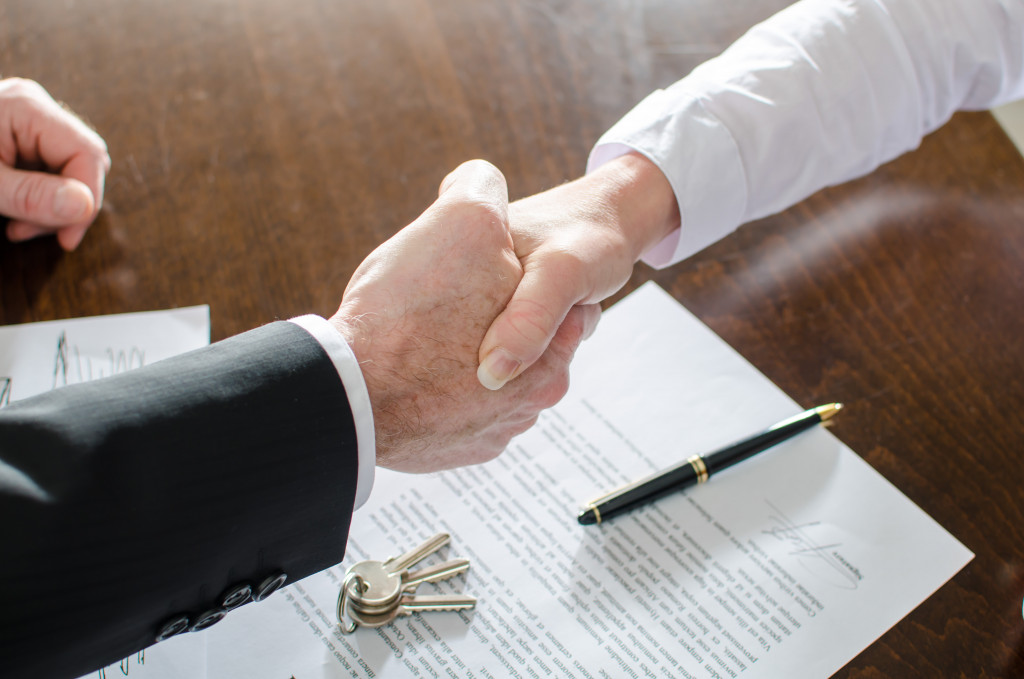 a businessman shaking hands with another man after signing a document and keys on the table