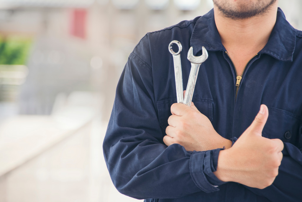 A mechanic holding wrenches and a thumb up