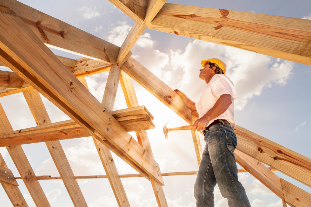 male roofer atop a roof frame with sky as background