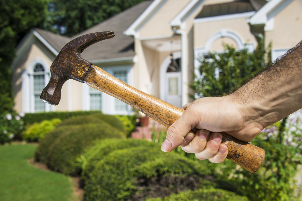 A hand holding a hammer in front of a house