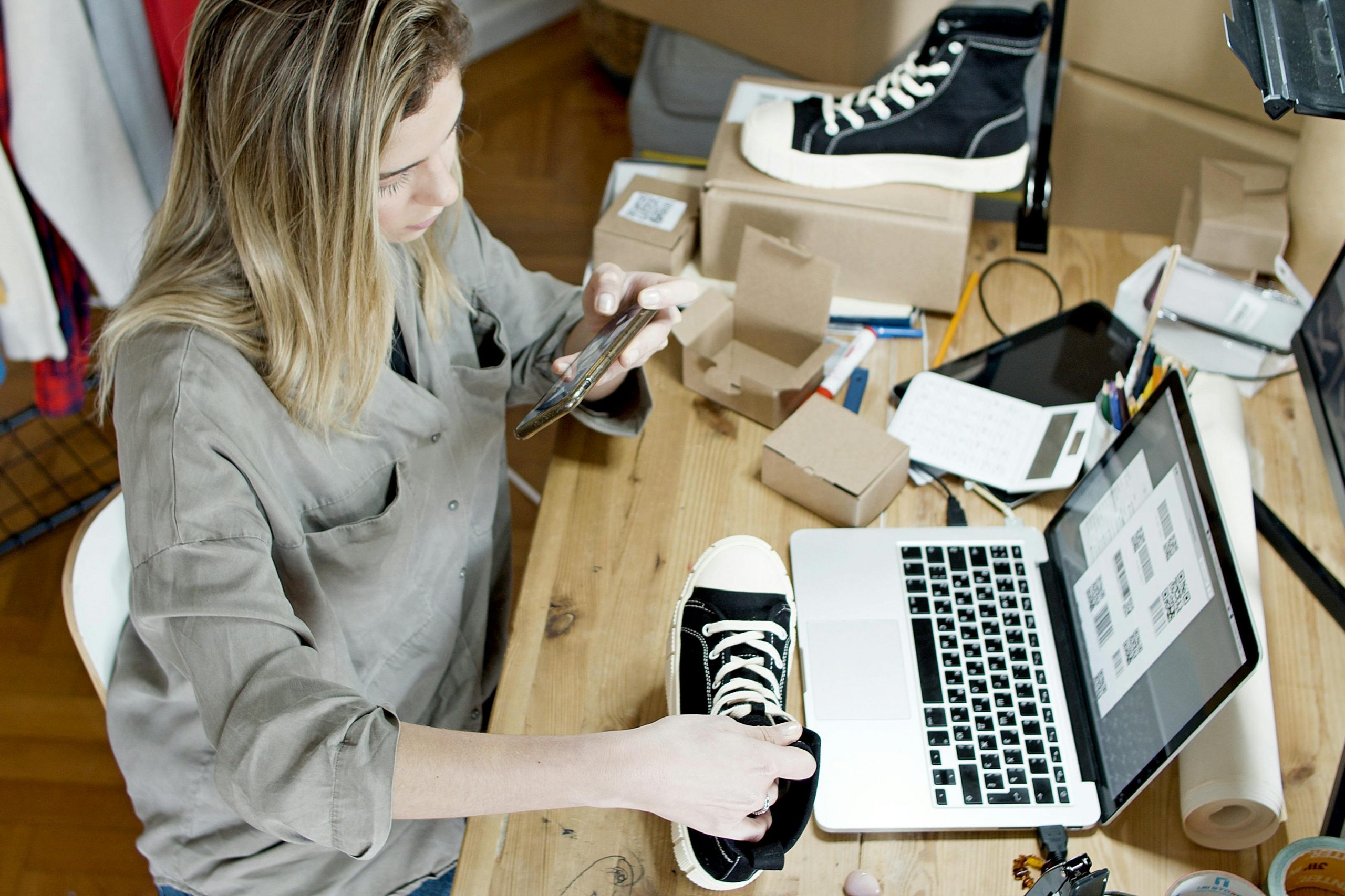 woman taking a photo of a black shoe at a desk with a laptop