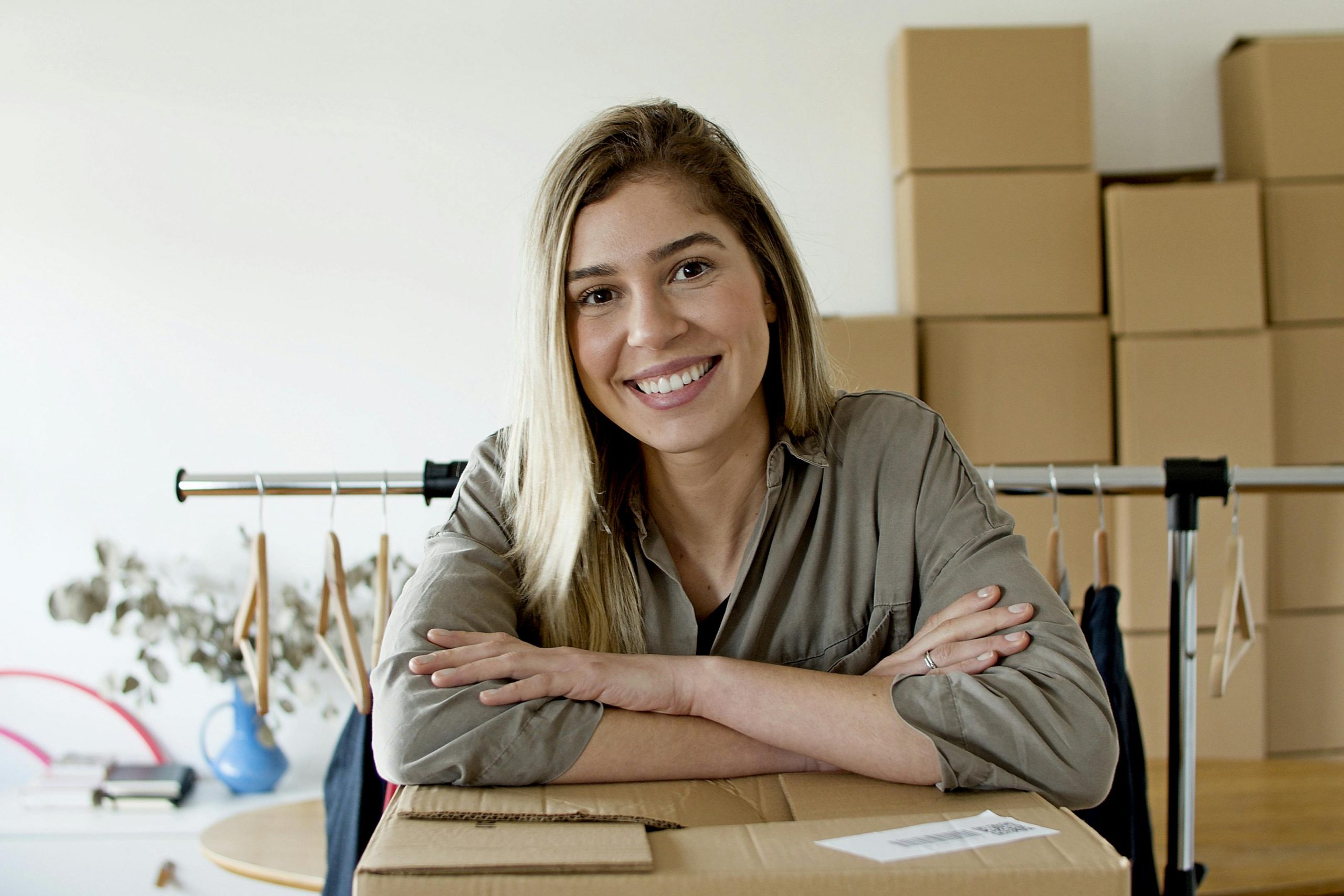 woman resting her arms on a cardboard box with a clothes rack and more cardboard boxes behind her