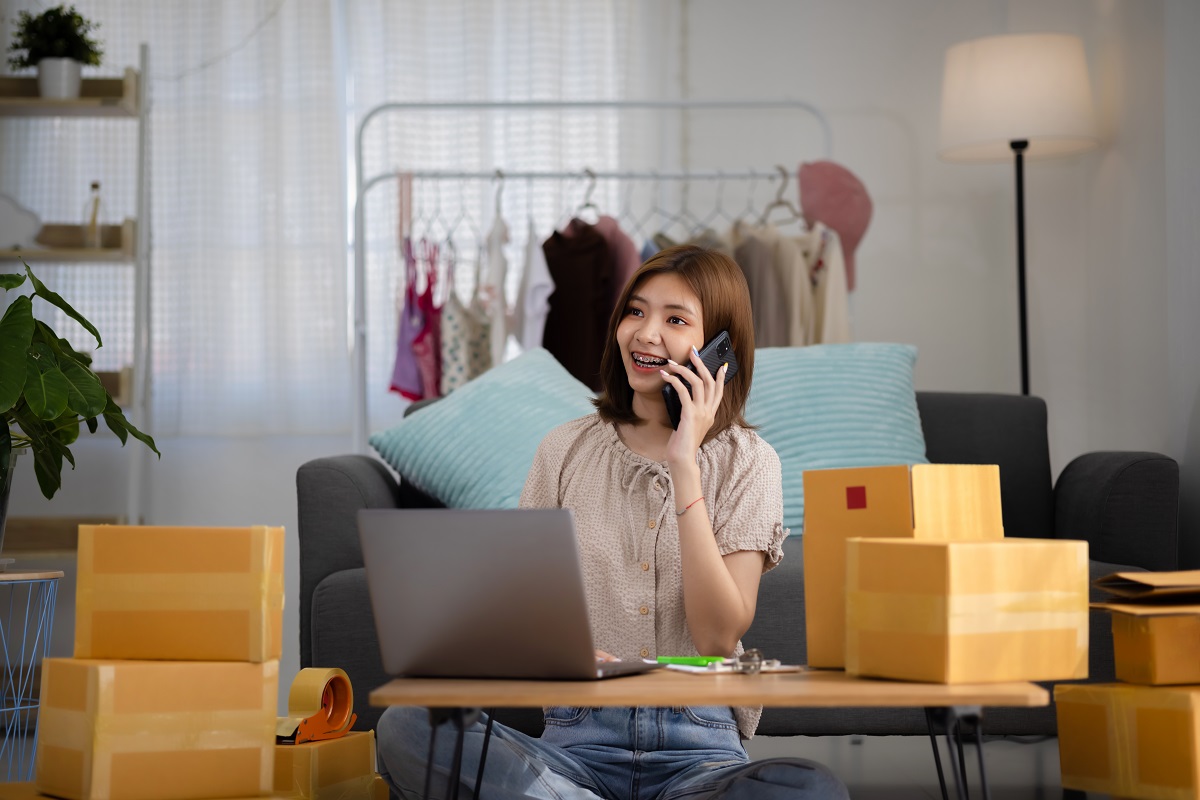 woman talking on her phone at a desk with a laptop and cardboard boxes